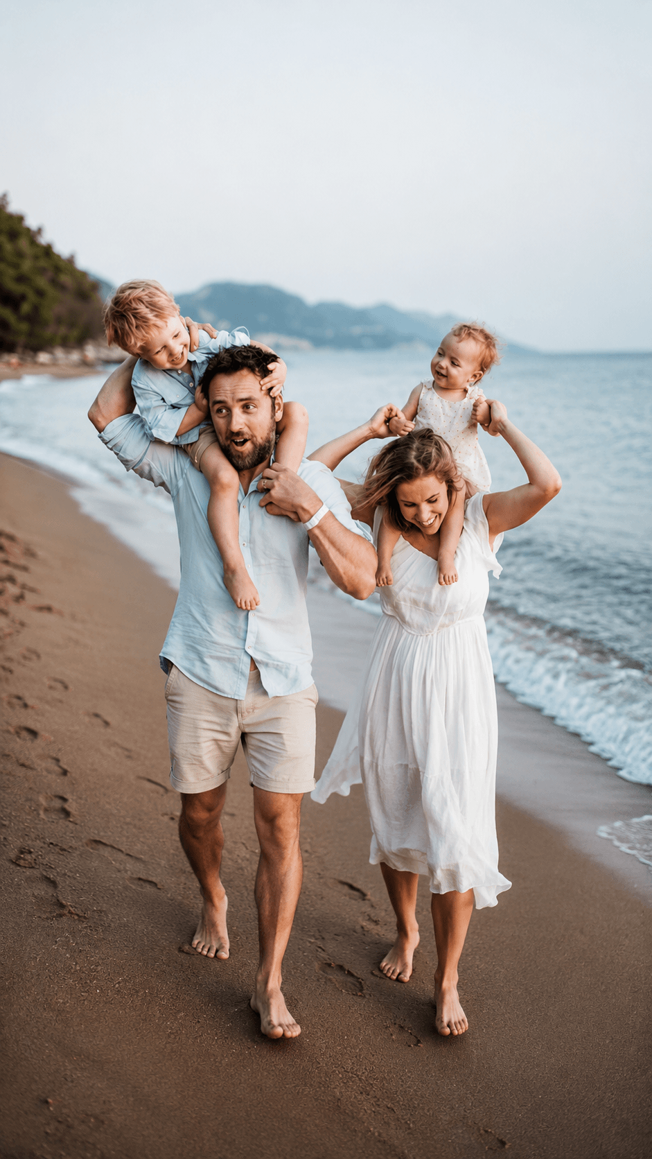 Family on a beach: parents carrying two young children on their shoulders near the water